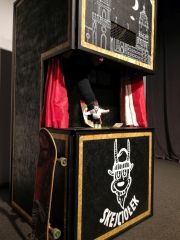 Zbliżenie na scenę, na której rozgrywa się historia Koziołka Skejciołka odgrywanego przez jednego aktora z pacynką . O scenę oparta jest deskorolka.