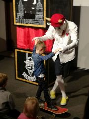 Koziołek Skejciołek pomaga ochotnikowi wybranemu z publiczności przejechać na deskorolce przez scenę.