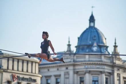 Kobieta robi szpagat na linie rozciągniętej między budynkami.