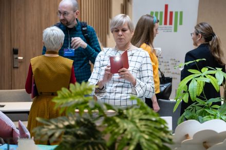 Przerwa kawowa. Ludzie rozmawiają na korytarzu. Jedna z pań robi zdjęcie kwiatom. 