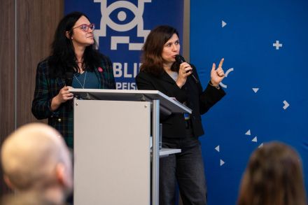 2 kobiety przemawiają do publiczności.