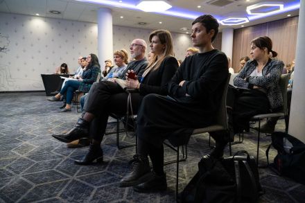 Publiczność siedzi na krzesłach i słucha.