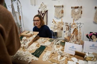 Na zdjęciu widać stoisko z makramami. Wystawca rozmawia z klientami.