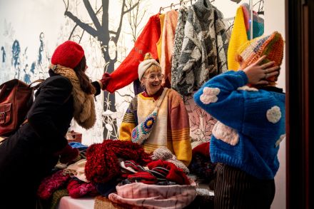 Dwie kobiety przymierzają wełniane czapki i  swetry.