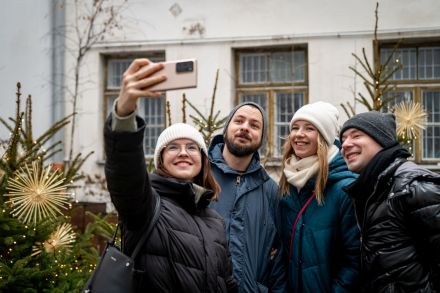Grupa młodych ludzi robi sobie zdjęcie na patio Warsztatów Kultury. Są tam choinki ze słomianymi gwiazdami.