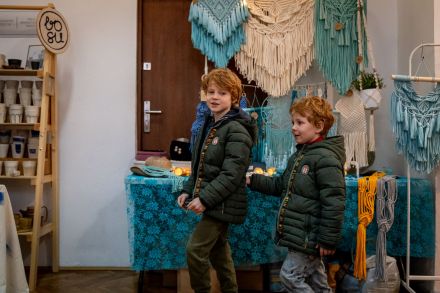 Dwóch chłopców uśmiecha się do aparatu. Przechodzą koło stoiska z makramą.