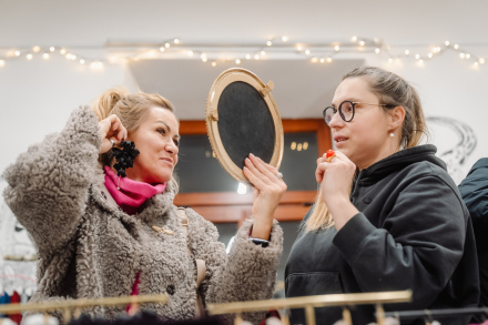 Dwie kobiety oglądają biżuterię. Jedna z nich ogląda się w lusterku.