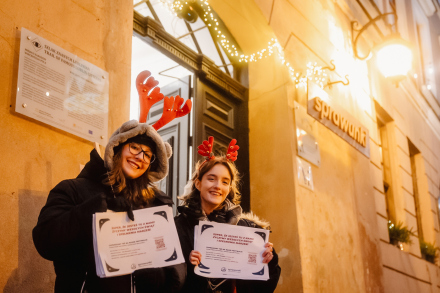 Wolontariuszki stoją przed kamienicą i zapraszają na Sprawunki.