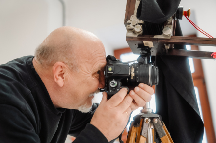 Starszy mężczyzna robi zdjęcie. Obok niego stoi aparat sprzed 100 lat.