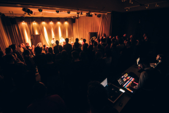 Widok na stół techników obsługujących wydarzenie, publiczność i rozjaśnioną scenę na której gra zespół Hańba.