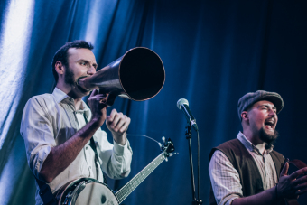 Dwóch członków zespołu wykrzykuje coś w stronę publiczności.