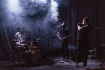 Na scenie znajduje się trzech muzyków: perkusista, basista i skrzypek. Scena jest zaciemniona. Unosi się dym. W sali panuje nastrój .