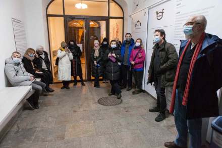 Trzy osoby siedzą, a pozostali stoją i słuchają prowadzących, którzy wypowiadają się na temat muralu.