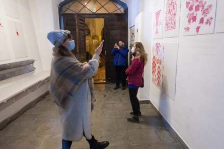 W korytarzu siedziby Warsztatów Kultury przy ul. Grodzkiej 7 stoją 3 osoby. Dwie z nich robią zdjęcia wystawie obrazów.