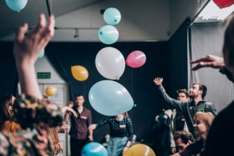 Zdjęcie ukazuje podrzucone, nadmuchane, różnokolorowe balony z imionami uczestników oraz samych uczestników.