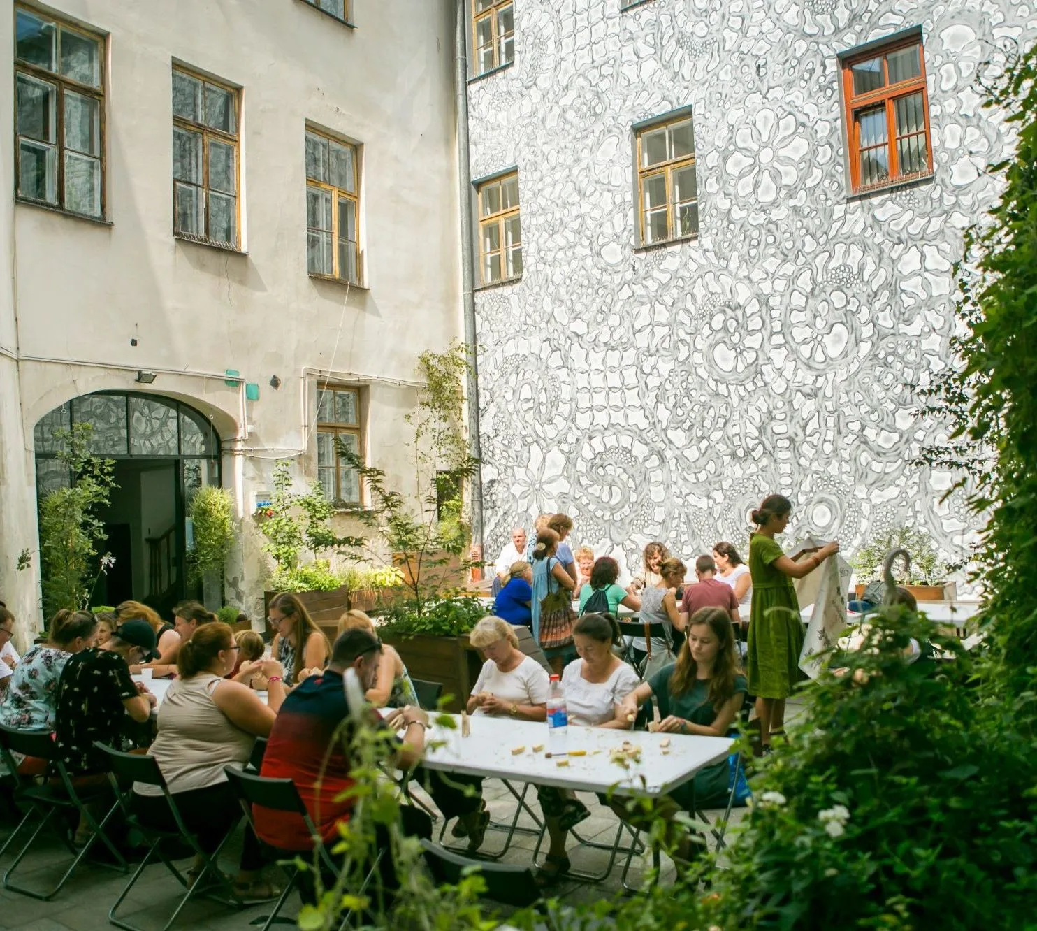 Patio kamienicy, w której siedzibę mają Warsztaty Kultury. Na patio, pośród zieleni rozstawione są stoły, przy których odbywają się warsztaty