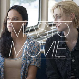 Na zdjęciu kadr z filmu. dwie kobiety siedzą obok siebie w autobusie lub innym środku transportu. Patrzą w okno. Na środku napis "Miasto Movie"