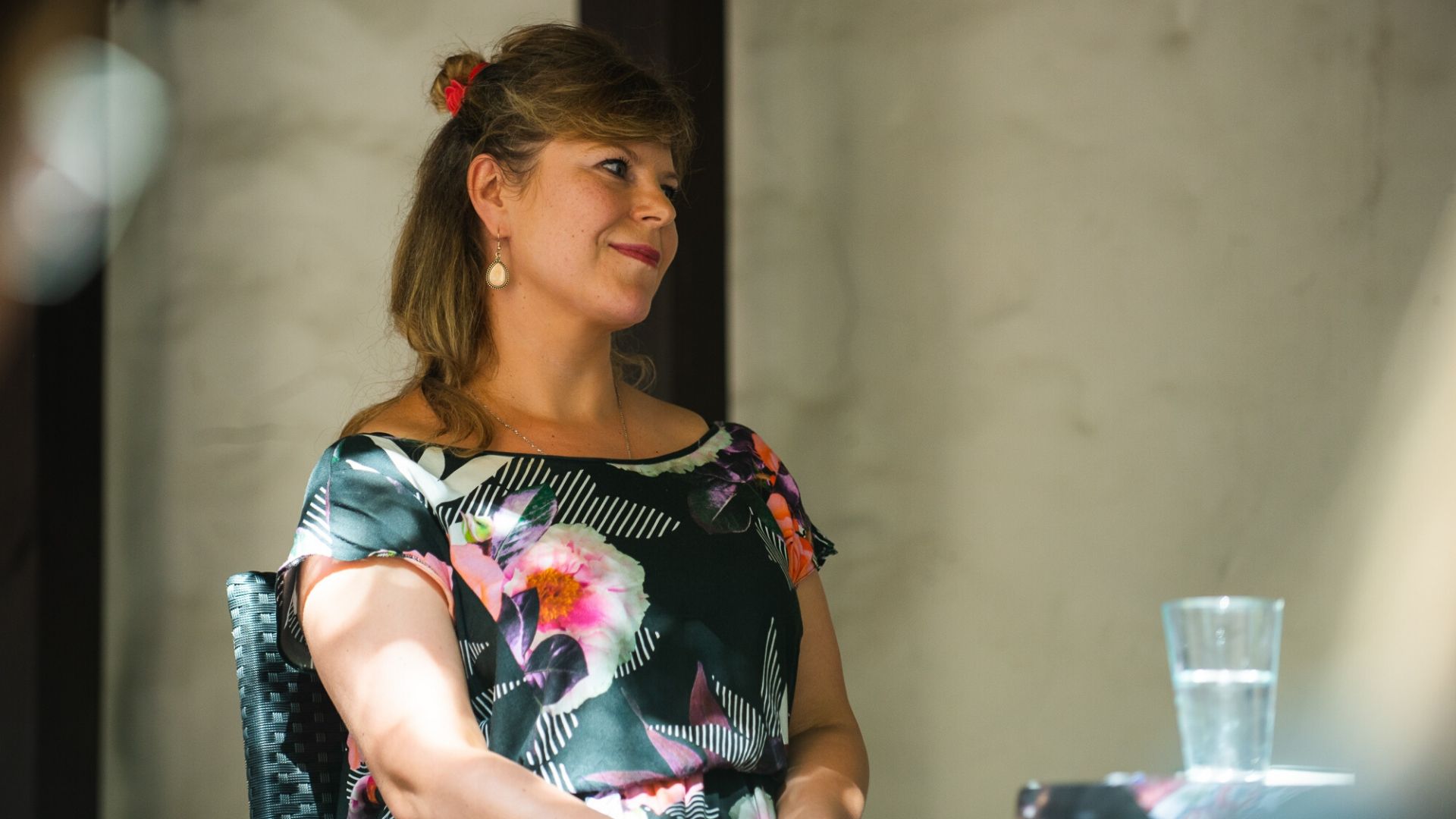 Aleksandra Zińczuk, prowadząca spotkanie literackie. Ubrana w kwiecistą sukienkę, wpatrzona w dal, poza kadr.