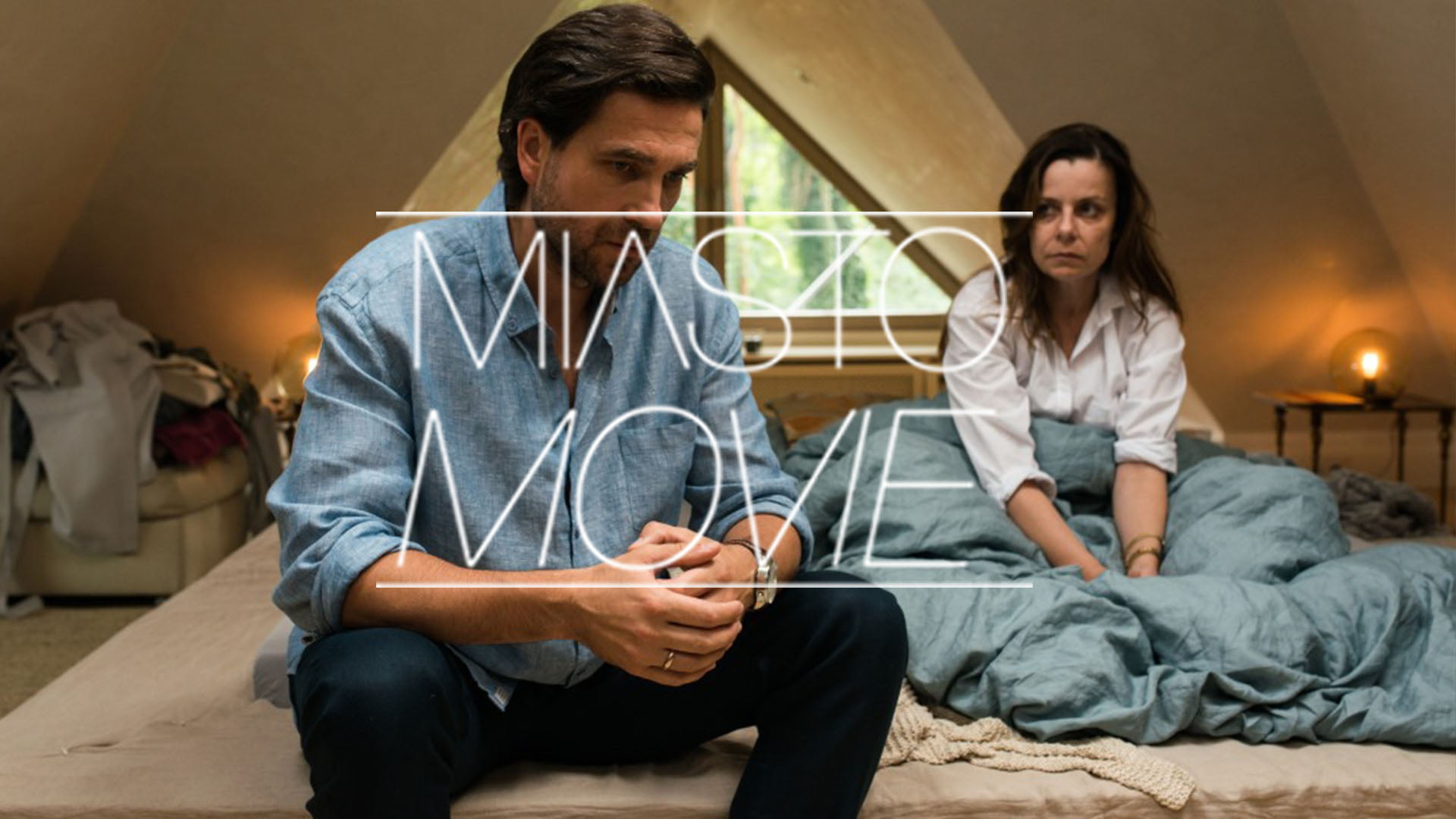 Kobieta i mężczyzna siedzą na łóżku. Na środku napis Miasto Movie.