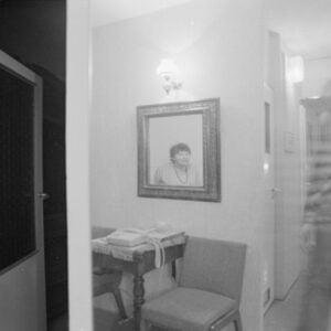 czarno-białe zdjęcie przedstawiające wnętrze domu. widoczny zarys osoby stojącej przy aparacie fotograficznym na statywie