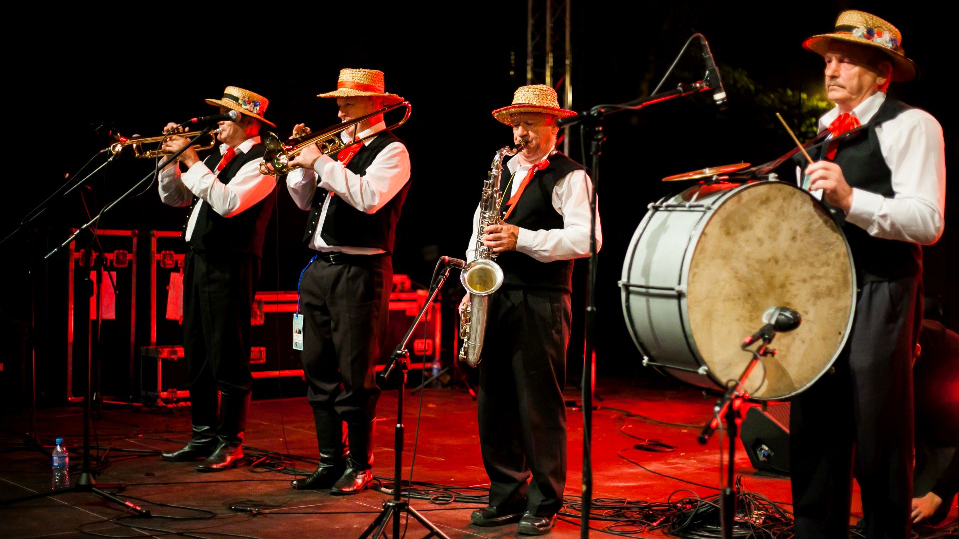 Grupa czterech mężczyzn ubranych w stroje ludowe, grających na instrumentach na scenie.