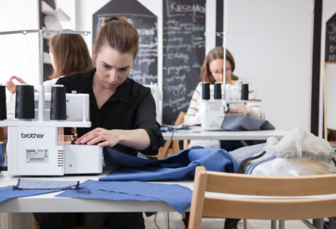 Zdjęcie przedstawia kobiety szyjące na maszynach do szycia.