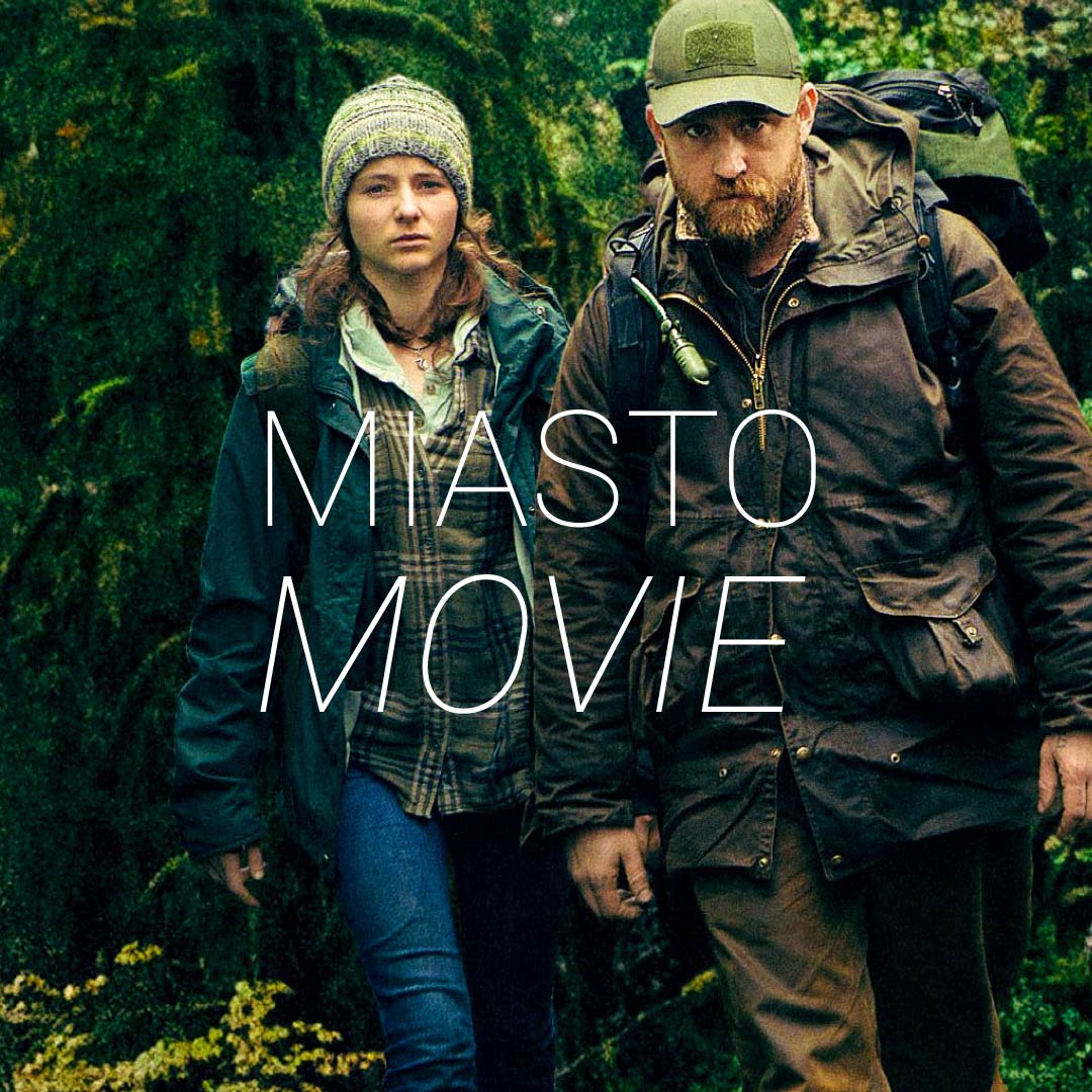 Zdjęcie przedstawia dwoje ludzi w lesie. Na środku napis Miasto Movie.