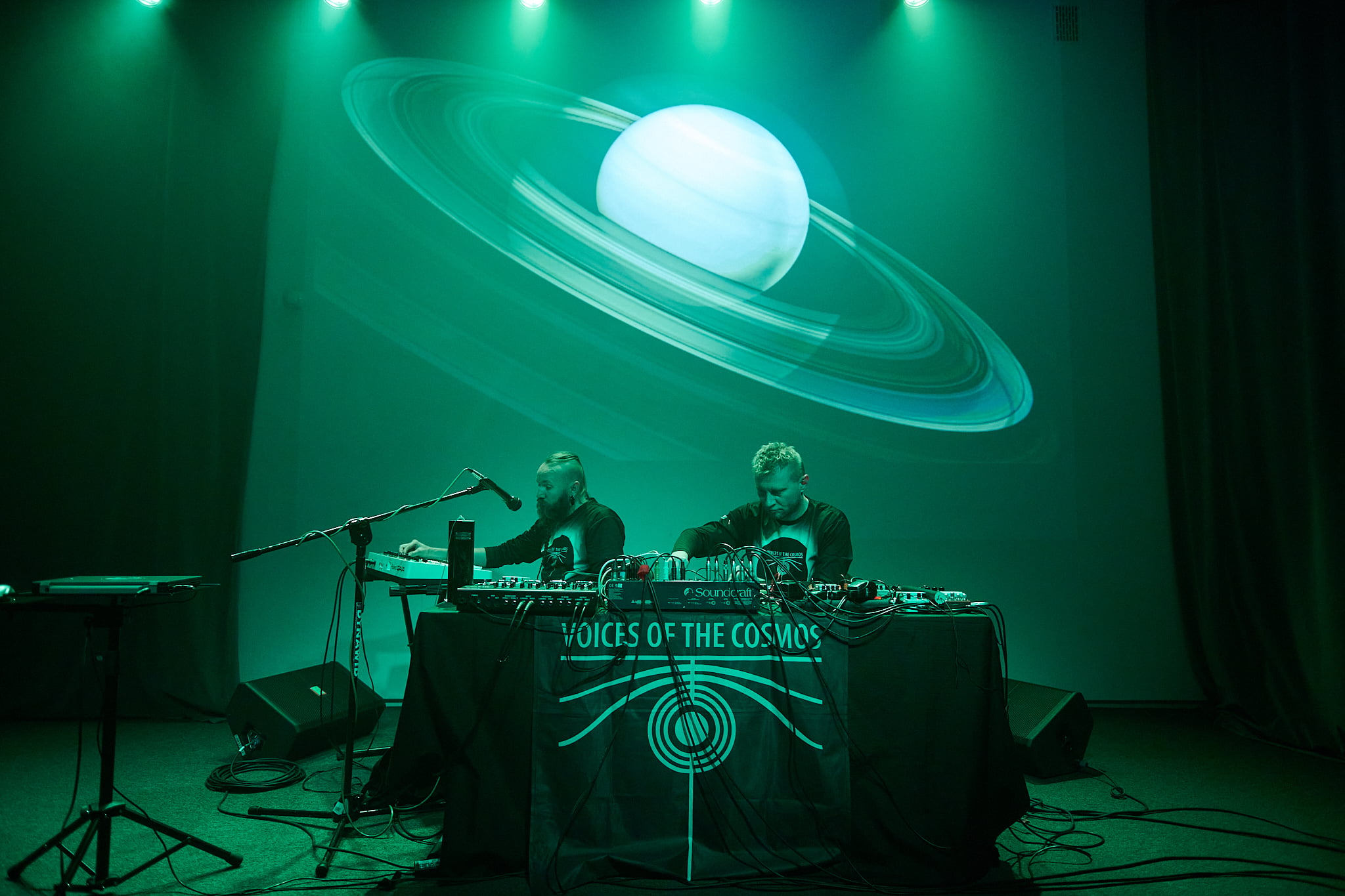 Two musicians on the stage. A planet is projected on the wall behind them, 