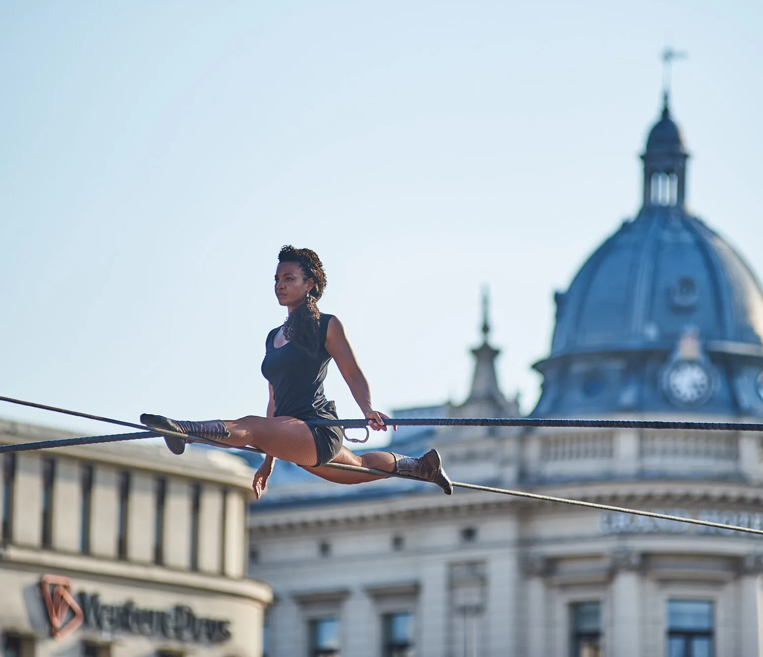 Kobieta robi szpagat na linie rozciągniętej pomiędzy budynkami Krakowskiego Przedmieścia.