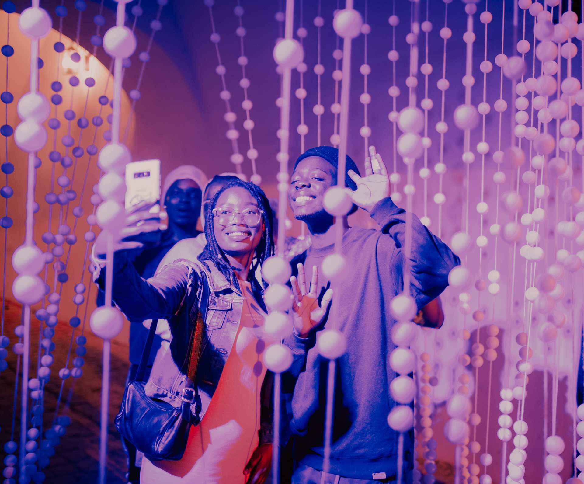 Dwie czarnoskóre kobiety robią sobie selfie wewnątrz jednej z instalacji artystycznych Nocy Kultury. Są to kandelabry wykonane z piłeczek pingpongowych nawleczonych na sznur.