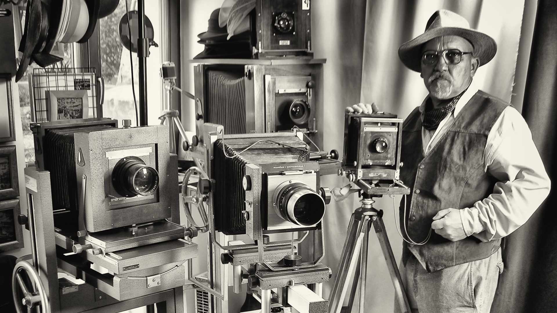 Czarno-białe zdjęcie fotografa Romana Krawczenki, który stoi przy pięciu aparatach analogowych.