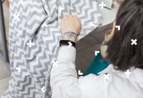 Fotografia kobiety siedzącej tyłem do obiektywu, która szyje na maszynie do szycia.