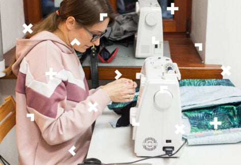 Młoda dziewczyna przedstawiona z profilu. Siedzi przy stole i szyje na maszynie.