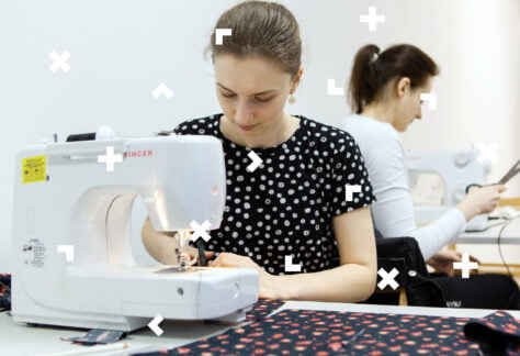 Kobieta siedzi przy maszynie i zszywa kawałki materiału.