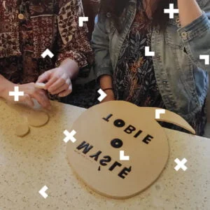 Dłonie dwóch kobiet, które siedzą przy stole i robią gliniane tabliczki z napisami.