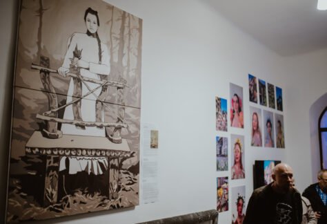 Wystawa na holu Warsztatów Kultury. Przedstawia obraz z młodą kobietą oraz fotografie dziewczyn, których twarze są pomalowane w kwiaty.