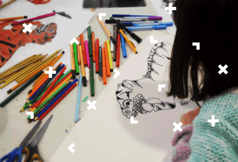 Dziewczynka maluje obrazek. Obok leżą kredki i flamastry,