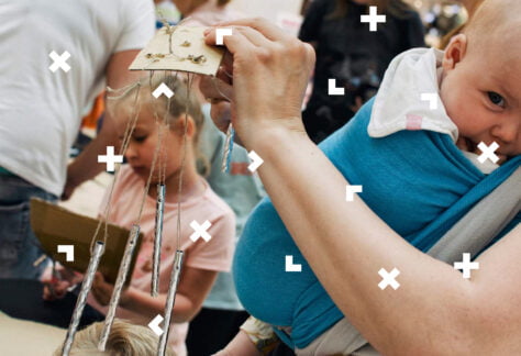 Kobieta buduje instrument. Na piersi ma zawinięte w chuście niemowlę.