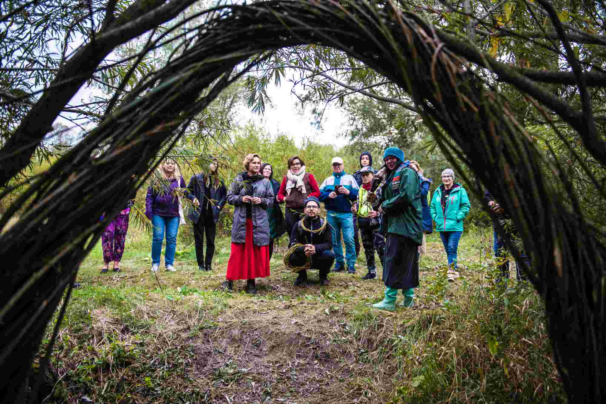 fot. Tomasz Tylus (124) Grupa ludzi stoi przy wiklinowej instalacji artystycznej, która przypomina łuk.