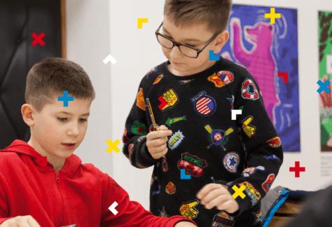 Jeden chłopiec siedzi przy stole, a drugi stoi obok niego.