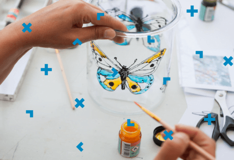 Kobieta maluje na słoiku motyla kolorowymi farbami.