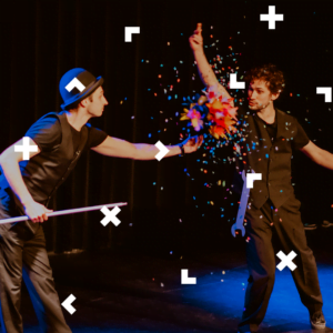 Dwaj mężczyźni na scenie. Jeden z nich trzyma kolorową kolę, z której wysypuje się confetti.