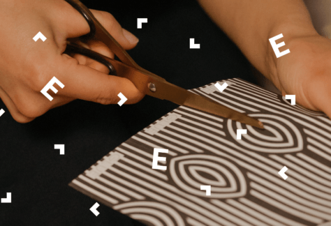 Zbliżenie na dłonie wycinające nożyczkami w biało brązowym, ozdobnym papierze.