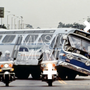 Kadr z filmu "LE MANS '66". Na jezdni stoi szereg samochodów wyścigowych. W ich kierunku biegnie kilka osób. Za samochodami stoi grupa ludzi. Na zdjęciu widnieje biały napis "Miasto Movie".