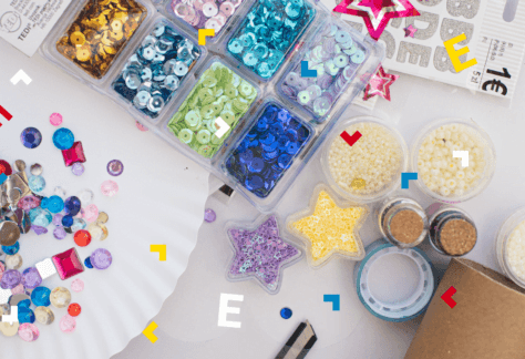 Na białym blacie leżą kolorowe cekiny, gwiazdki, taśmy, papiery i naklejki.