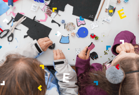 Przy białym stole siedzą mała dziewczynka i kobieta. Wycinają z filcu kształty. Na stole leżą nożyczki, igły, ołówki, szablony, cekiny.