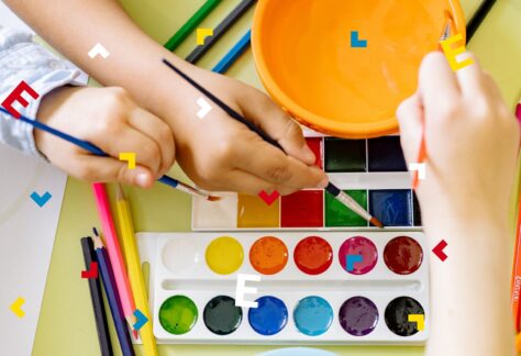 Dzieci trzymają w dłoniach pędzelki i malują farbami.