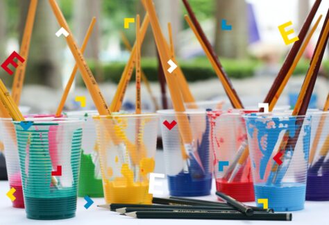 Kubeczki z wodą zabrudzoną farbami. Moczą się w nich pędzle.