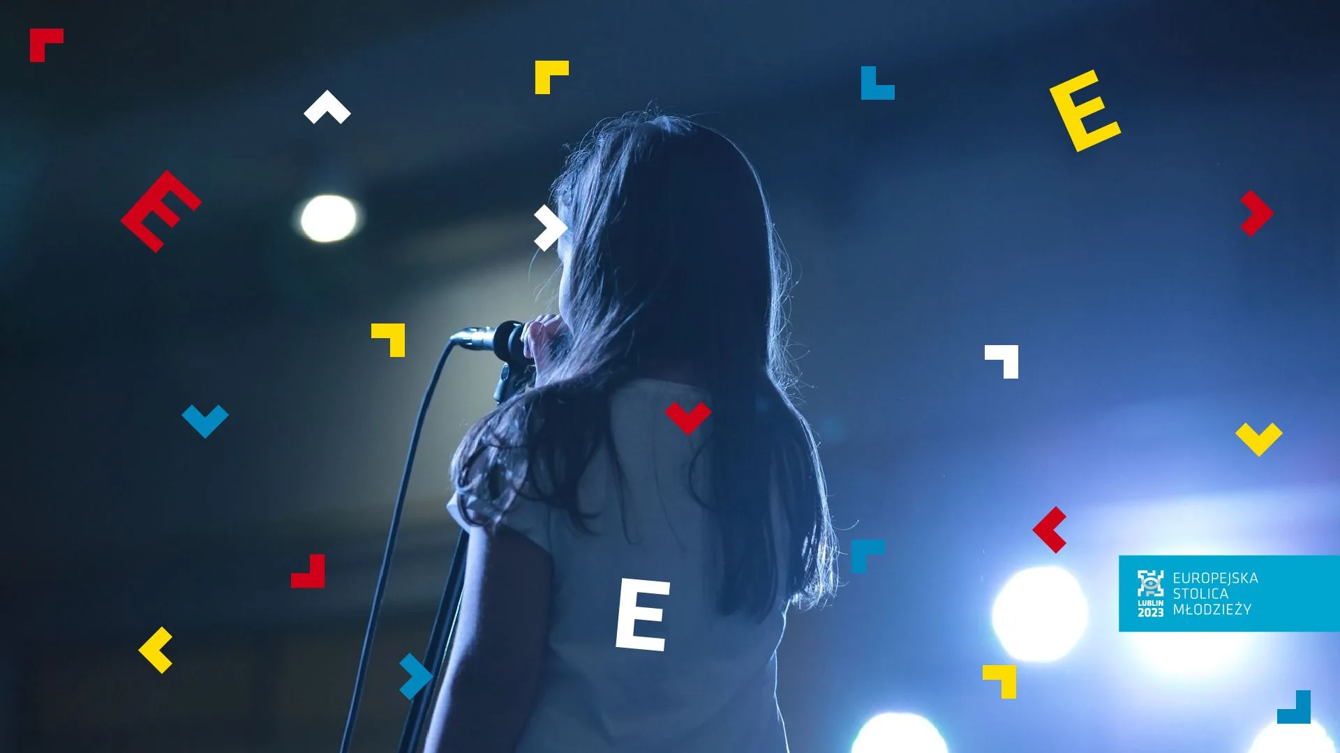 Dziewczynka stoi tyłem przy mikrofonie.