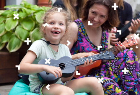 Mama z córką uczą się grać na ukulele. Patrzą w stronę instruktora.